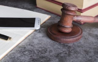 Fotografia colorida de martelo de juiz, smartphone e livros jurídicos.