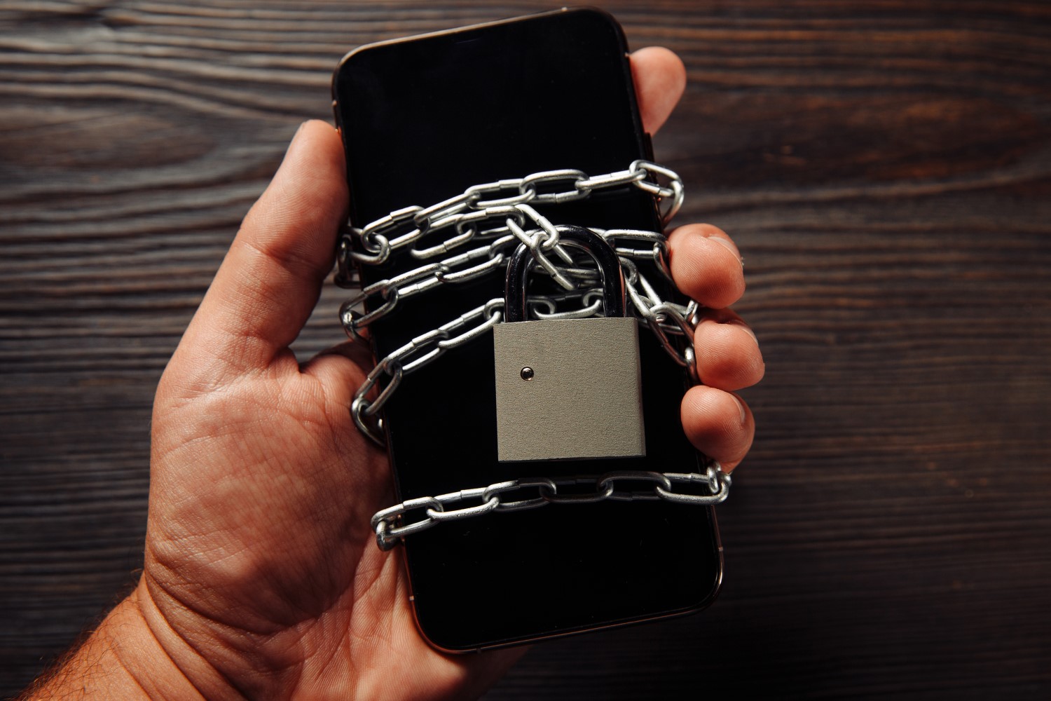 Imagem de uma mão segurando um celular envolto em correntes e um cadeado.
