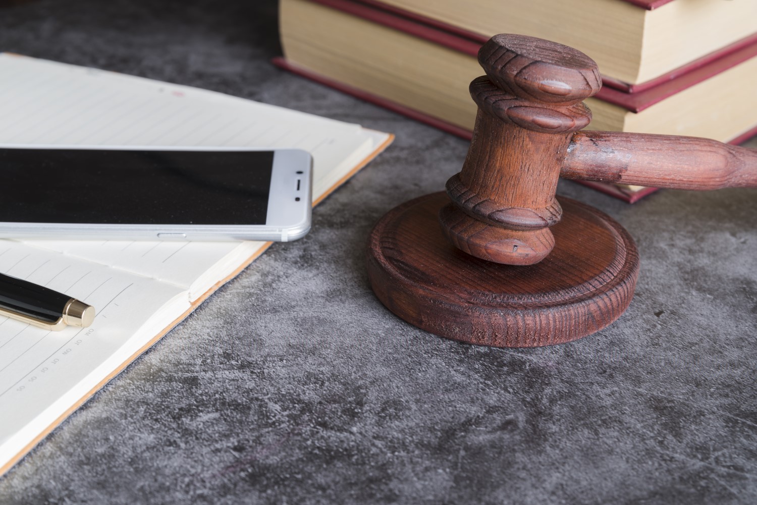Fotografia colorida de martelo de juiz, smartphone e livros jurídicos.